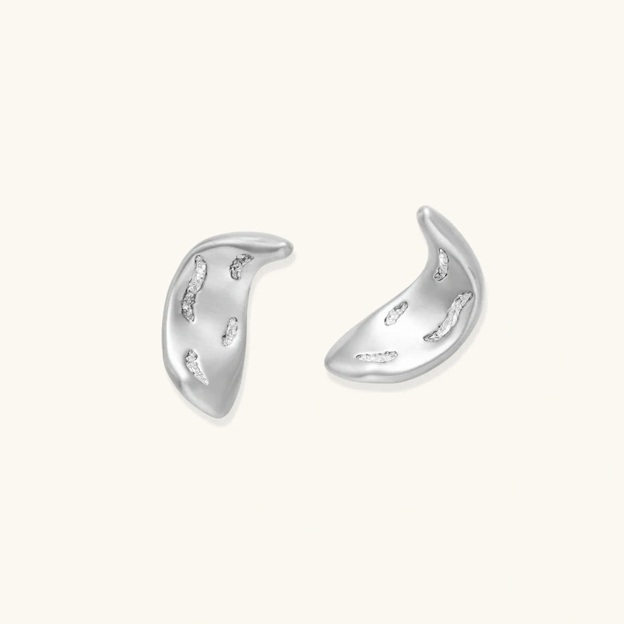 Curved crescent-shaped earrings in gold and silver with scattered perforated details on neutral background.
