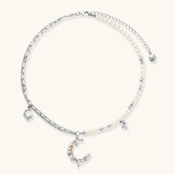 Silver-toned crescent moon pendant with star accents on pearl and chain necklace against white background.