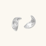 Curved crescent-shaped earrings in gold and silver with scattered perforated details on neutral background.