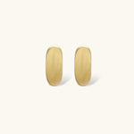 Small gold huggie earrings with matte finish, 14mm diameter, shown against cream background for everyday elegance.