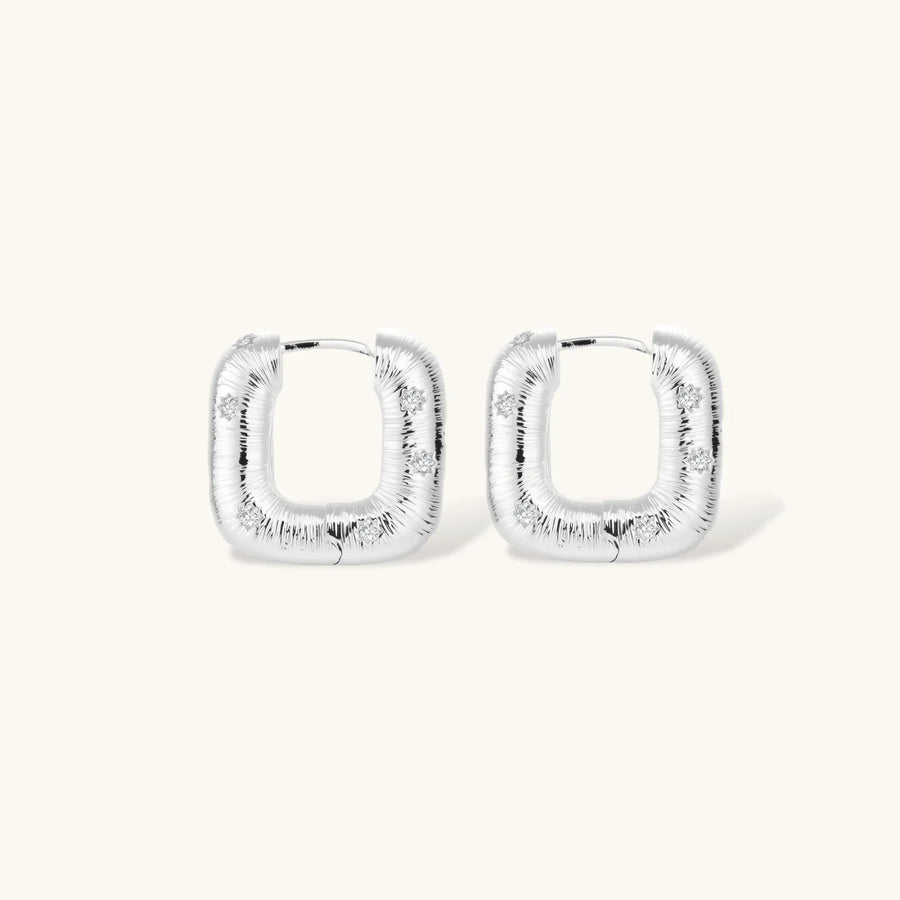 Close-up of ridged silver-plated hoop earrings with embedded crystal details on white background.