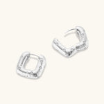 Close-up of ridged silver-plated hoop earrings with embedded crystal details on white background.