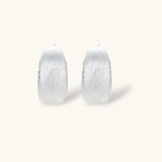 Close-up of small silver-plated hoop earrings with brushed texture and a row of sparkling zircon crystals on white background